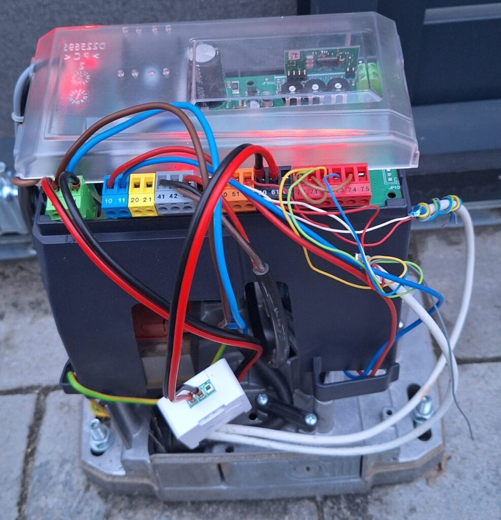 Kapunyitó motor vezérlőegység belső képe: színes vezetékek, sorkapcsok, átlátszó burkolat alatti áramköri lap, számozott csatlakozási pontokkal (pl. 10, 20, 41, 60, 75, ...)